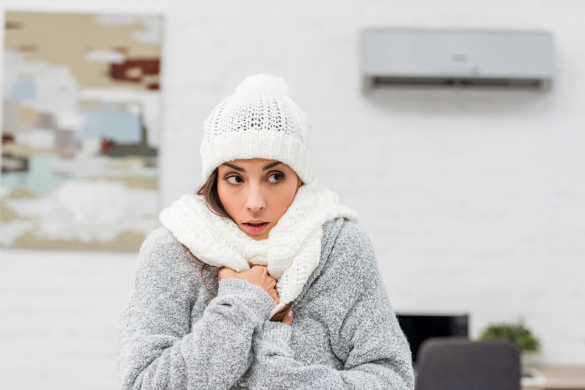 woman wearing jacket, hat and scarf inside because furnace is broken